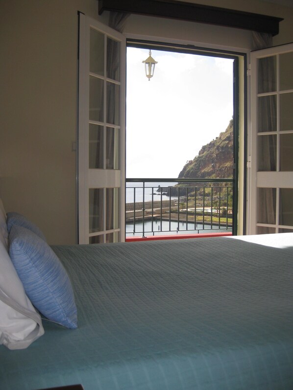 Un dormitorio con cama, almohadas y vistas a un balcón con barandilla y un colgador de luz.