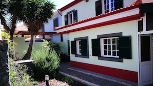 Una casa de fachada roja y blanca, techo de tejas y jardín con diversas plantas y flores.