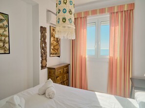 Une chambre à coucher avec un lit, une commode en bois, un luminaire suspendu et une fenêtre avec des rideaux.