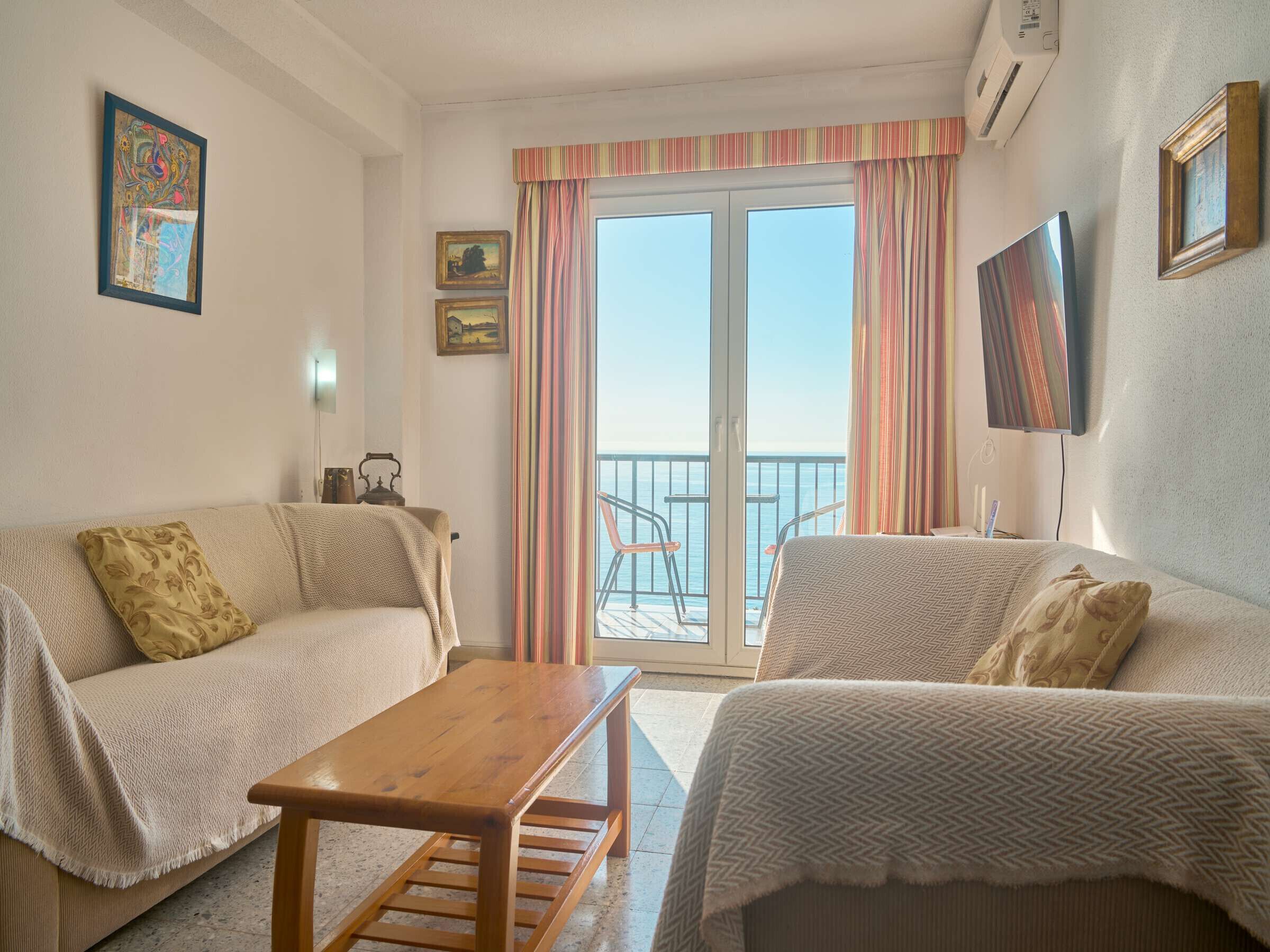Une pièce comprenant un canapé, un banc en bois, une télévision et un balcon avec une balustrade.
