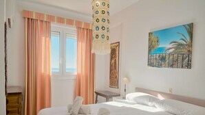 Ein Hotelzimmer mit einem Bett, einem Fenster mit Vorhängen, einem Strandbild und einer Lampe.