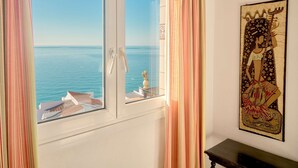 Ein Zimmer mit Meerblick, ein Fenster mit Vorhängen und ein an der Wand hängendes Gemälde.