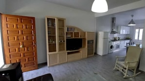Un ambiente compatto con un armadio in legno, un televisore, una poltrona a dondolo e un angolo cottura con lavatrice.