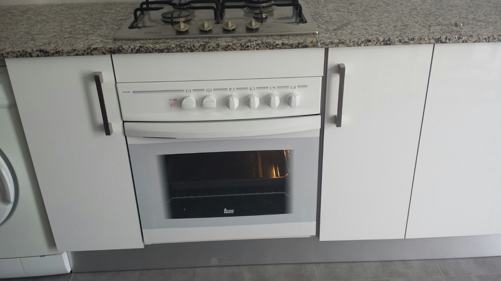 A kitchen with a gas stove, oven, and white cabinets.