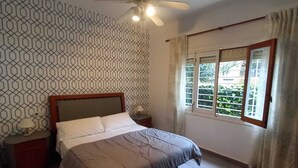 Una camera da letto con un letto, una ventola a soffitto, una finestra con tende e un muro decorato.