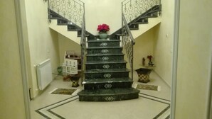 Una escalera con barandilla de metal decorativa, un jarrón con flores en la parte superior y una pequeña mesa con un jarrón en la plataforma.