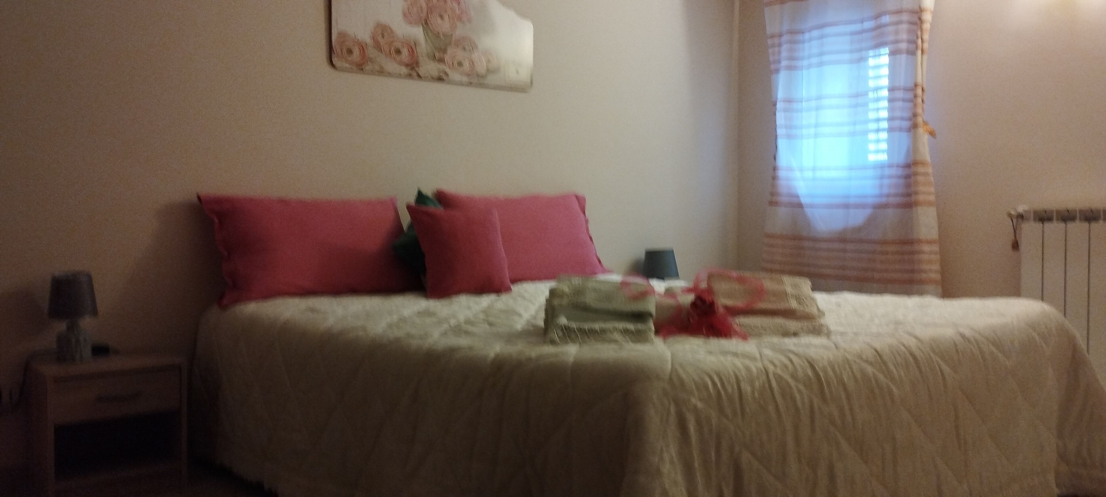 Una cama con ropa de cama roja y blanca, una mesita de noche con una lámpara y una ventana con cortinas.
