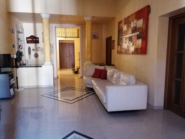 A spacious living area with a white sofa, a television, and a kitchen area in the background.