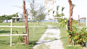 A pathway leading to a wooden archway with a sign, surrounded by greenery and palm trees. - Evasion (Gressier)