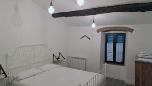 A bedroom with a white bed, a radiator, a window with blinds, and a wooden ceiling beam. - Farmhouse on an Organic Farm (Carmignano)