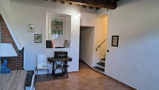 A narrow hallway with a staircase, a small table with a chair, and a shelf with books and a bottle. - Farmhouse on an Organic Farm (Carmignano)