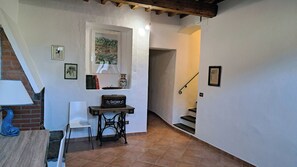 Un estrecho pasillo con una escalera, una pequeña mesa con una silla y un estante con libros y una botella.