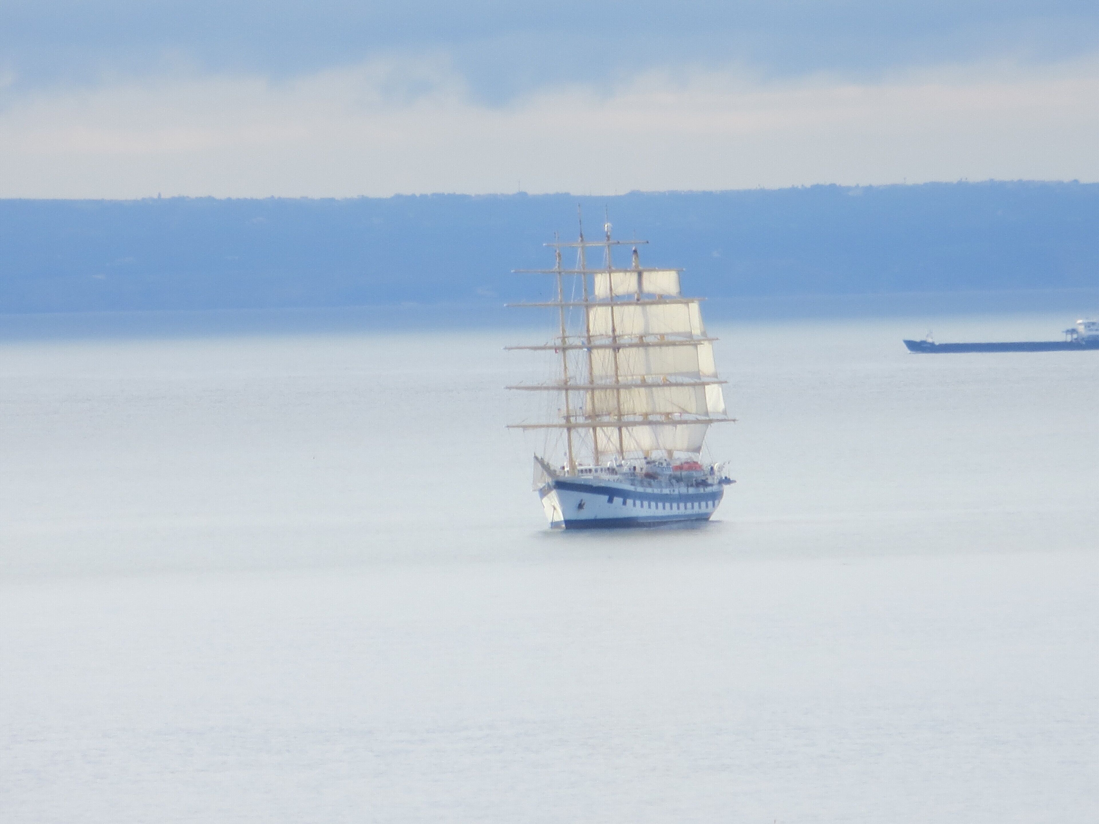 Een groot zeilschip op rustig water met een verre kustlijn.