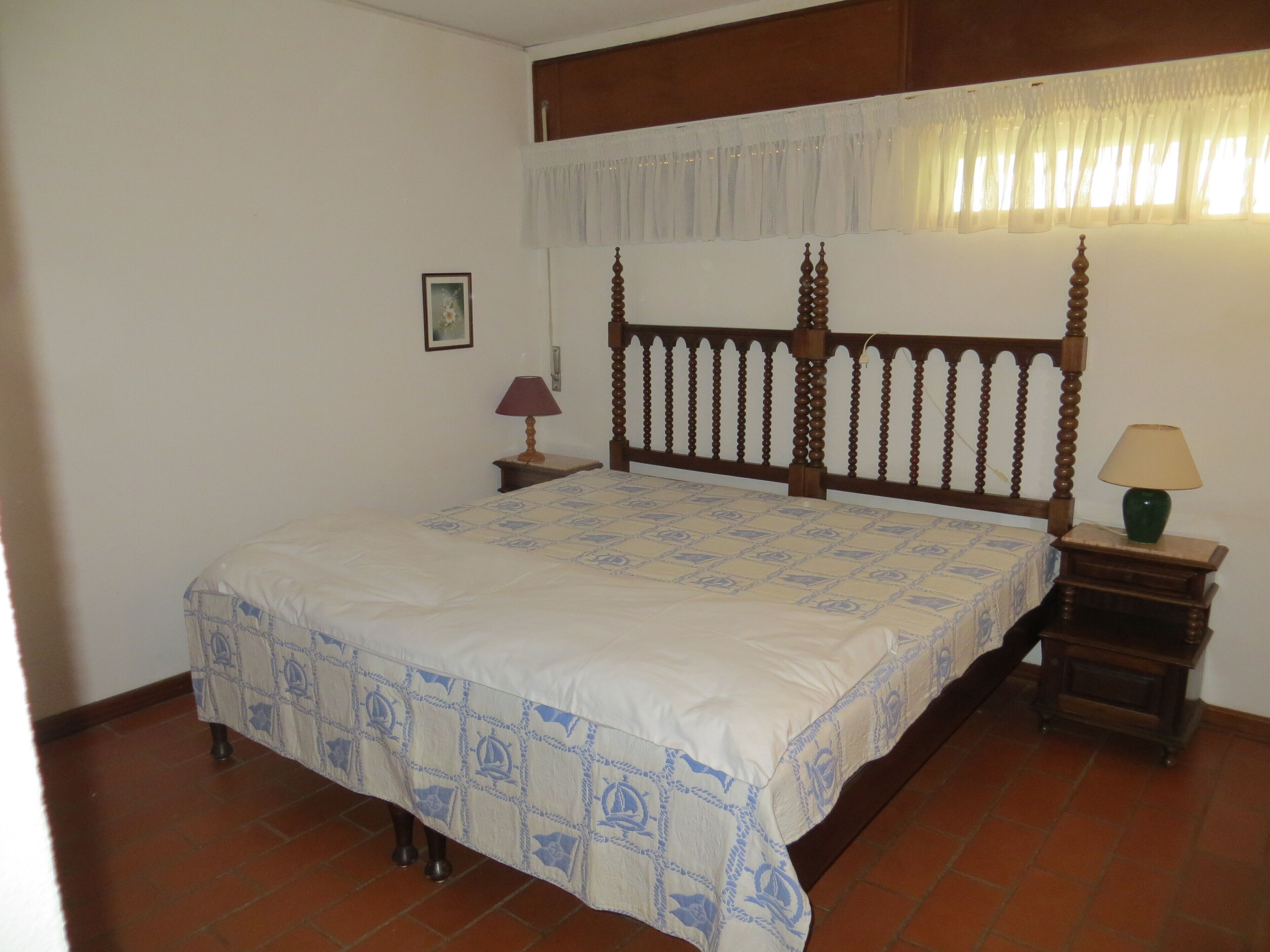 A bedroom with a wooden four-poster bed, a nightstand with a lamp, and a small bedside table with a lamp.