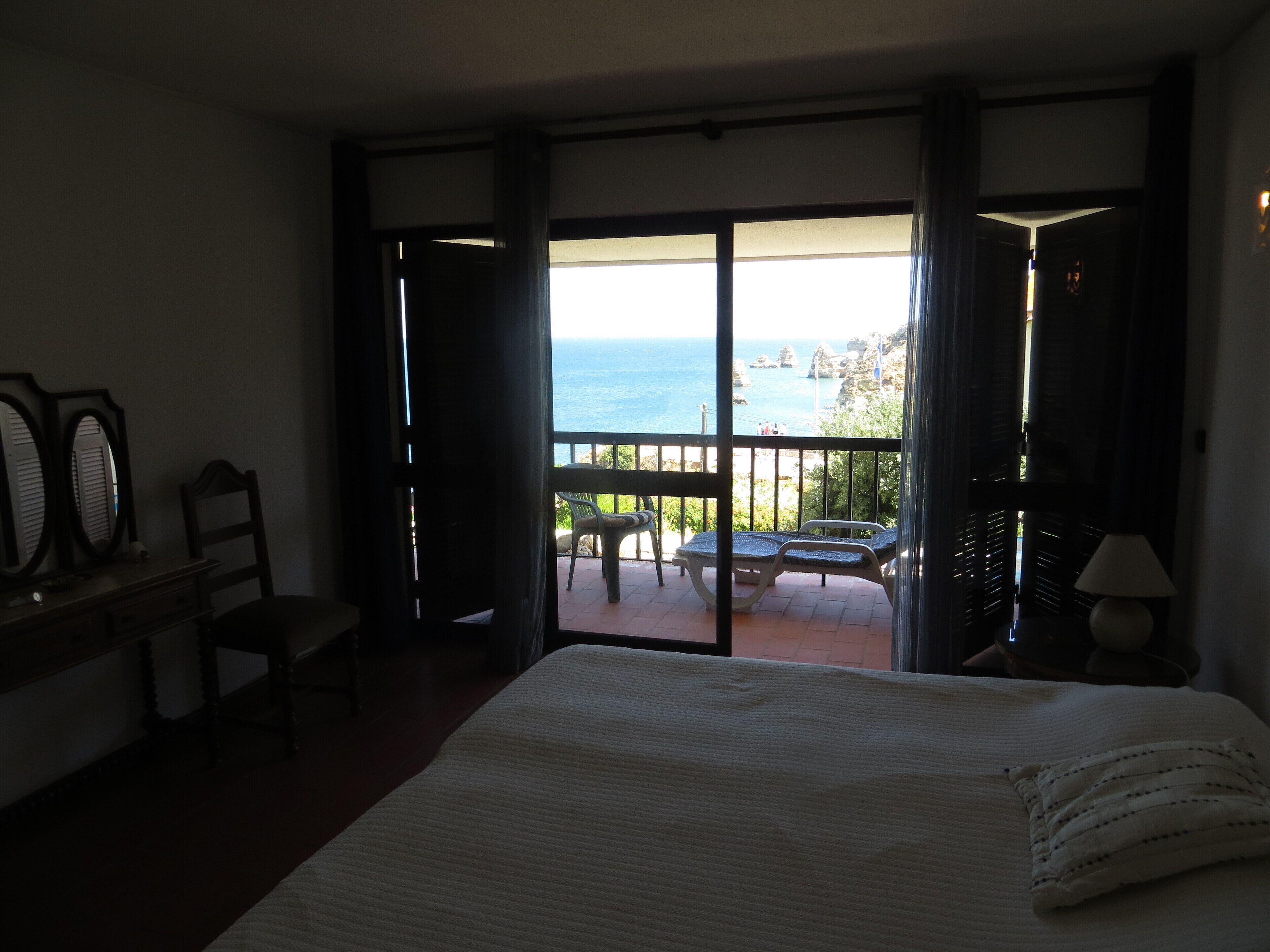 A hotel room with a bed, a desk, a chair, and a balcony with a view of the sea.