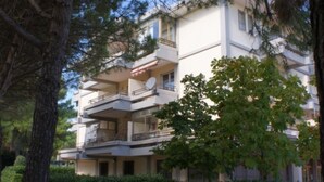 A multi-story residential building with balconies, a satellite dish, and a well-maintained hedge. - Peaceful flat in Bibione (Bibione)