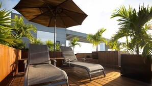 Een dakterras met twee ligstoelen, een parasol en plantenpotten.