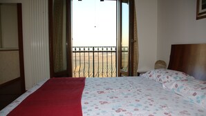 Un dormitorio con cama, una manta roja, una colcha estampada con motivos florales y vistas al exterior a través de una puerta corredera.