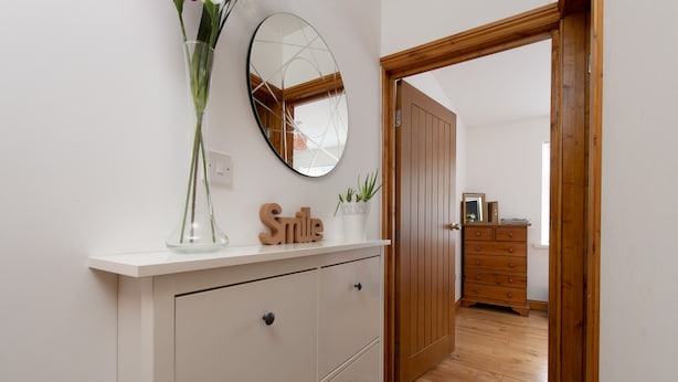 A hallway with a white dresser, a mirror, a vase with green plants, and a wooden door leading to another room. - Modern Apartment "Woodleigh" Sleeps 4 (London)