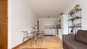 A modern kitchen with white cabinets, a dining area with clear glass chairs, and a grey sofa. - Modern Apartment "Woodleigh" Sleeps 4 (London)