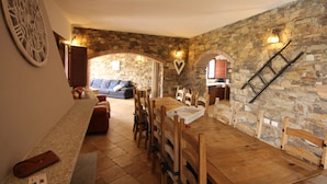 A dining area with a stone wall, wooden furniture, and a large clock. - Exceptional villa: 400 m²  for 15 people, with pool (Tertenia)