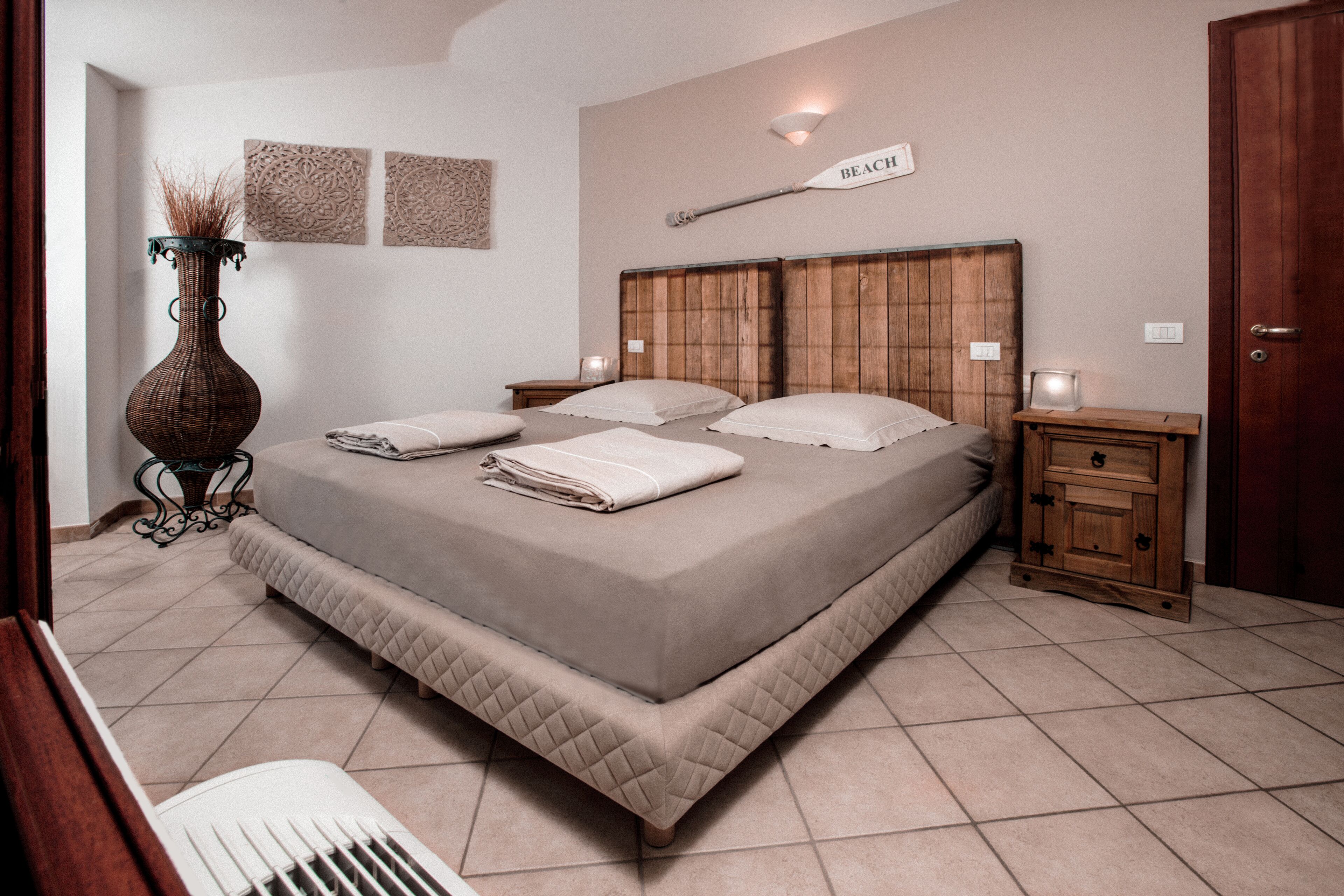 A bedroom with a large bed, bedside tables, a nightstand, a vase, and wall decor.