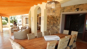 A wooden dining table with wicker chairs, a hanging light fixture, and a stone wall in the background. - Exceptional villa: 400 m²  for 15 people, with pool (Tertenia)
