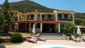 A two-story building with a pool area, outdoor seating, and a mountain backdrop. - Exceptional villa: 400 m²  for 15 people, with pool (Tertenia)