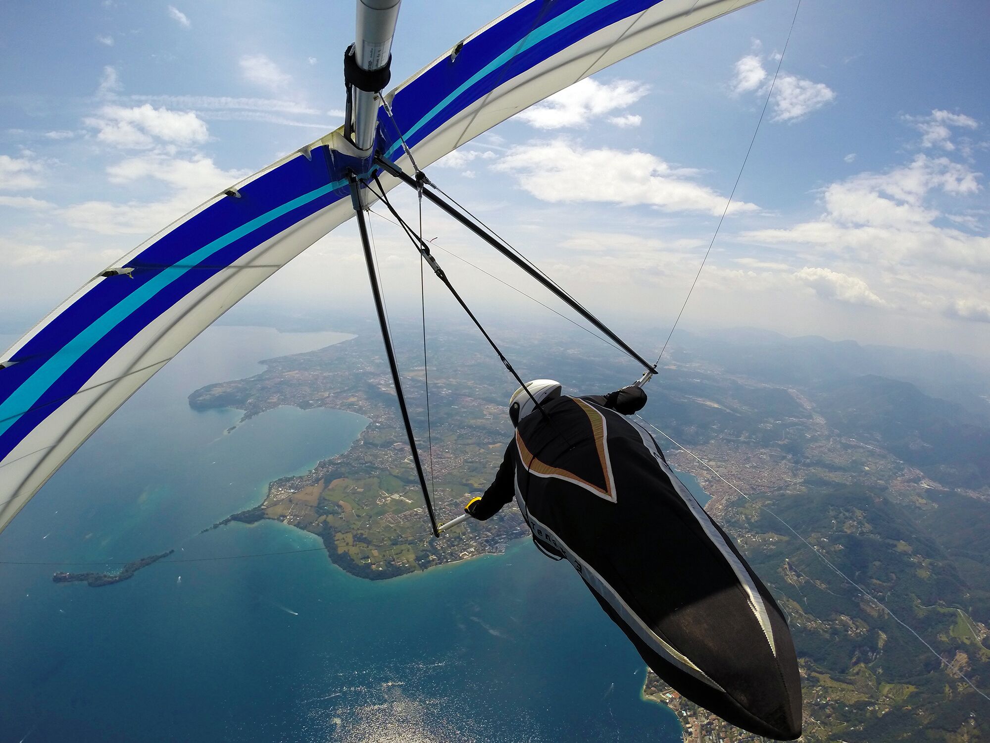 Un parapente aux ailes bleues et blanches, survolant un paysage côtier où l’on distingue la terre et l’eau.