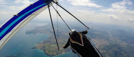 Un parapente aux ailes bleues et blanches, survolant un paysage côtier où l’on distingue la terre et l’eau.