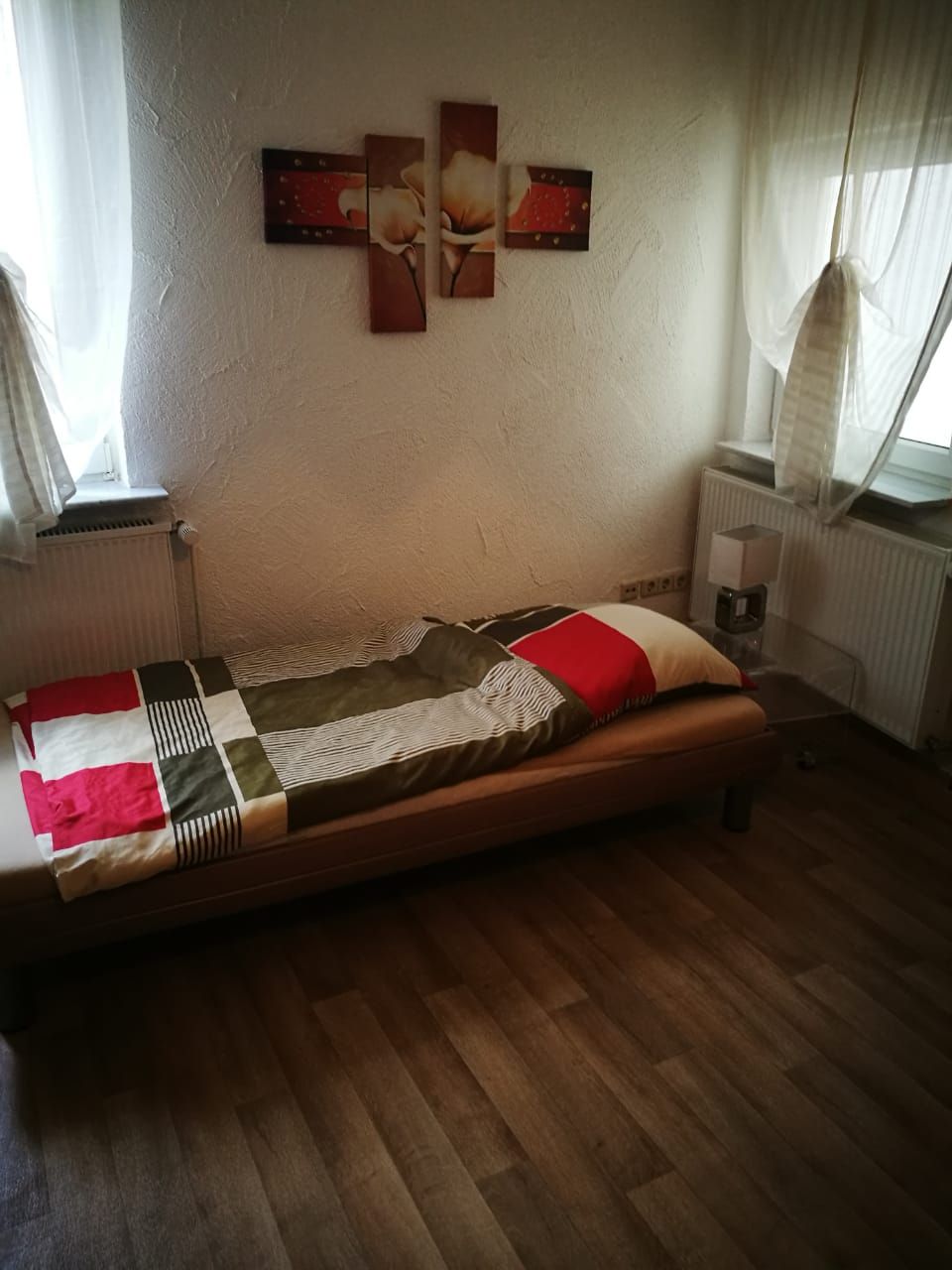 Een eenpersoonsbed met een bedsprei met dessin, een nachtkastje met lamp en een radiator.