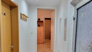 A hallway with a wooden door labeled "WC" on the left, a tiled floor, and a staircase leading to a room with a wooden door and a small cabinet. - Vacation apartment Kiefer in Hillscheid near Koblenz (Hillscheid)