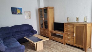 A living room with a blue sofa, a wooden entertainment unit, and a television. - Vacation apartment Kiefer in Hillscheid near Koblenz (Hillscheid)