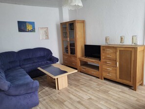 A living room with a blue sofa, a wooden entertainment unit, and a television. - Vacation apartment Kiefer in Hillscheid near Koblenz (Hillscheid)