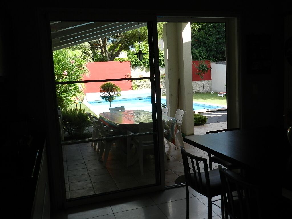 Une pièce dotée d’une porte-fenêtre coulissante donnant sur une terrasse avec une piscine, du mobilier d’extérieur et une vue sur un bâtiment rouge.