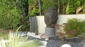 Een tuin met een Boeddhabeeld, omringd door grind, witte kiezels en groene planten.