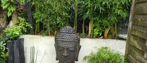 A garden with a Buddha statue, surrounded by bamboo, ferns, and a stone lantern.