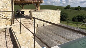 Un bâtiment en pierre avec un toit en tuiles, des places assises à l’extérieur et un espace piscine.