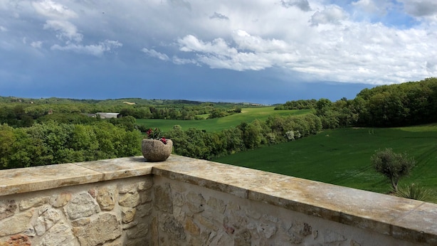 Une balustrade en pierre surplombe un paysage verdoyant et luxuriant, sous un ciel dégagé.