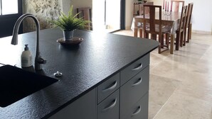 Une cuisine avec un mur en pierre, un évier, une plante en pot et un coin repas comprenant une table et des chaises.