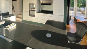 A modern kitchen with a skylight, built-in appliances, and a dining area with black chairs. - Quiet house with garden - Golfe du Morbihan (Baden)