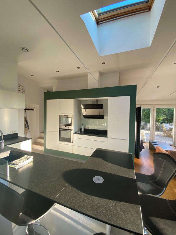 A modern kitchen with a skylight, built-in appliances, and a dining area with black chairs.