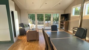 A spacious living area with a large sliding glass door leading to a deck, a dining table with chairs, and a built-in kitchen area. - Quiet house with garden - Golfe du Morbihan (Baden)