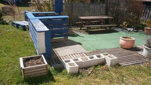 En baghave med træterrasse, en forhøjet plantebed, et picnicbord og en stor terracotta krukke.