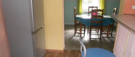 A compact kitchen with a refrigerator, a dining table with chairs, and a blue stool.