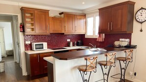 Una cocina con armarios de madera, una encimera blanca, un microondas, una tetera y un reloj en la pared.