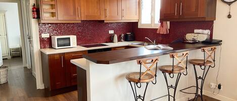 A kitchen with wooden cabinets, a white countertop, a microwave, a kettle, and a clock on the wall.