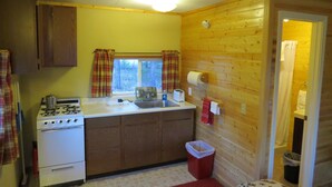 Una cocina compacta con paredes de madera, estufa, pileta y una ventana con cortinas.