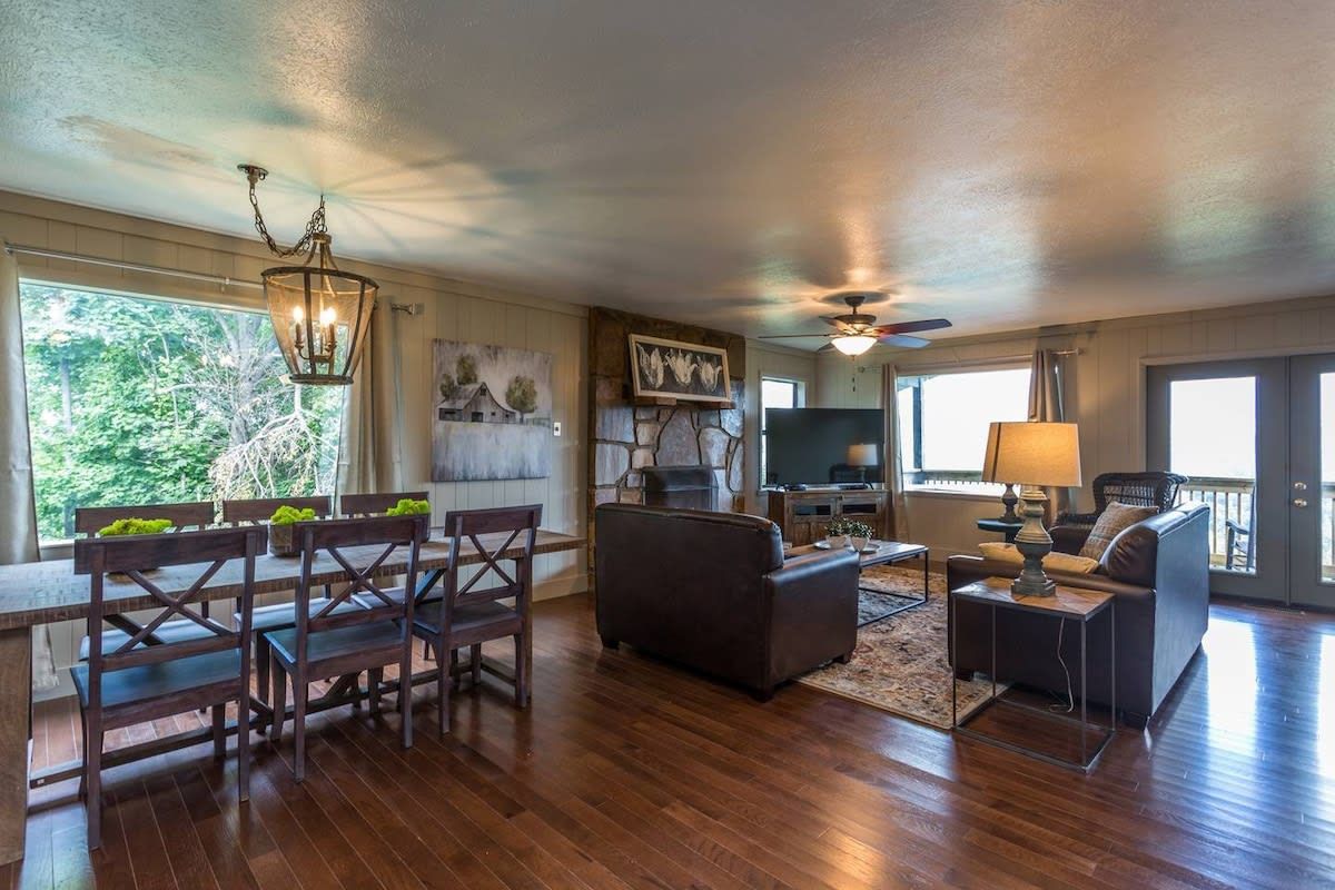 A spacious living room with a wooden dining table, dark sofas, and a television.