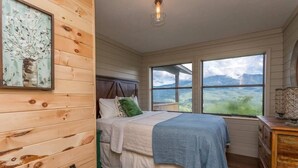 A bedroom with a bed, a window with a view, a wooden headboard, and a framed picture on the wall.